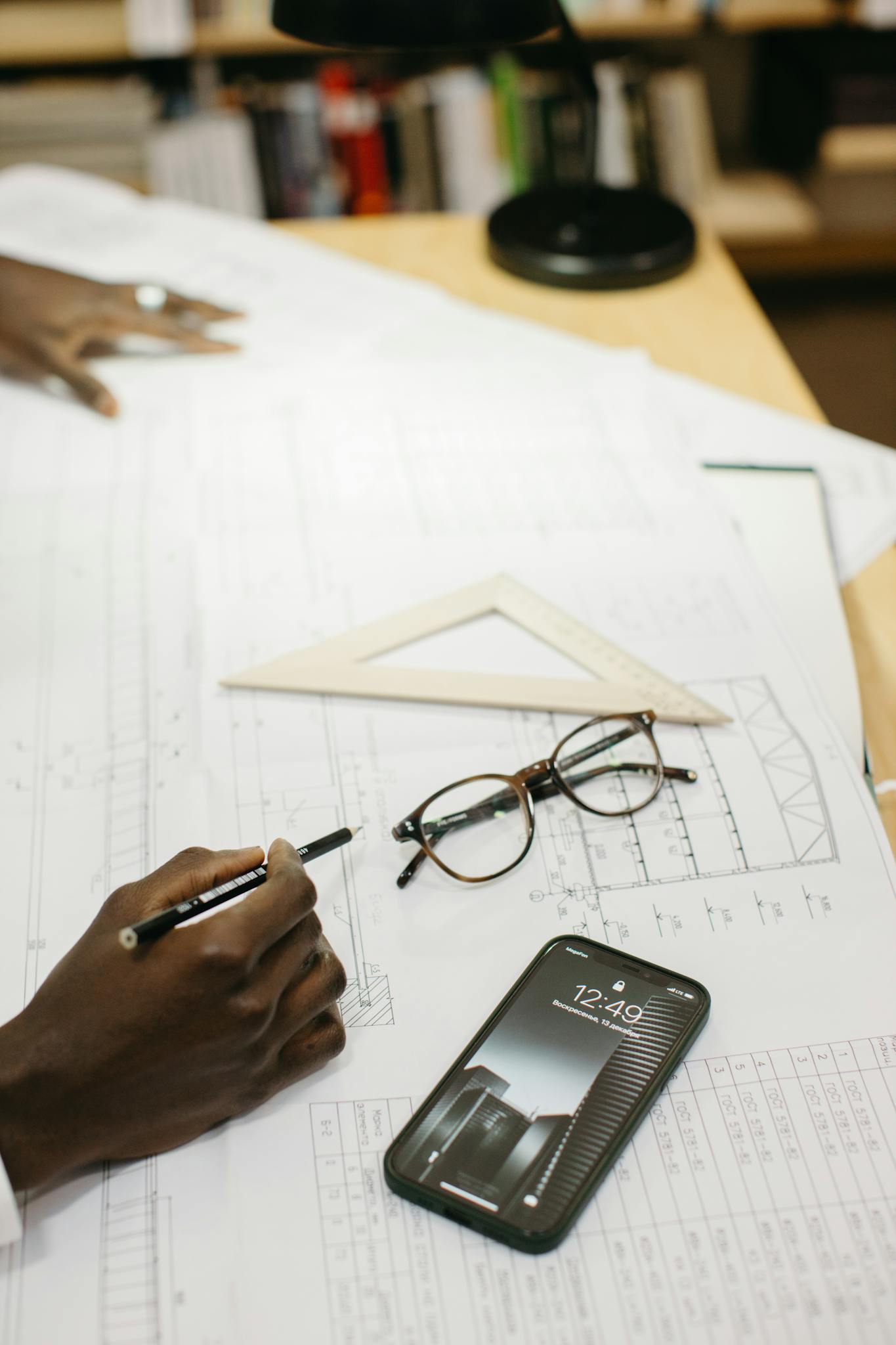 An architect working on blueprints in a modern office with a smartphone and glasses on the desk.