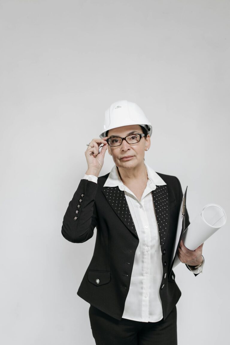 Professional female architect wearing a hard hat holding blueprints, on a neutral background.